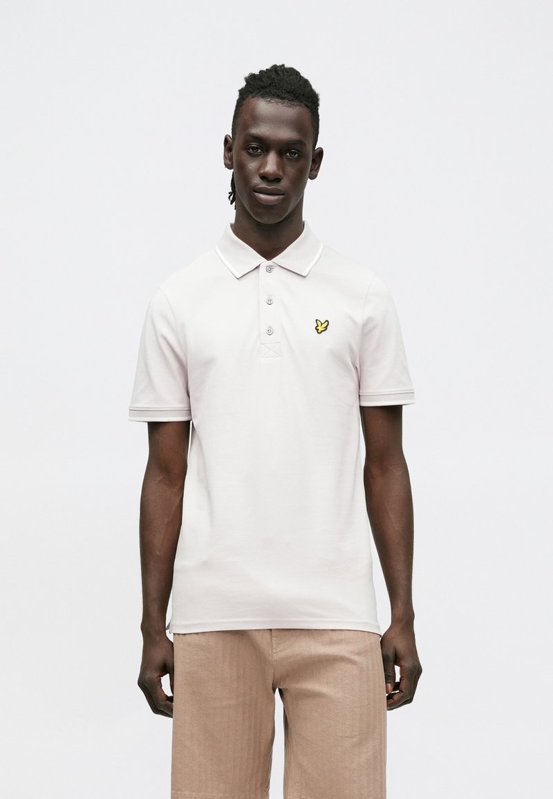 Lichtroze poloshirt met kraag, drieknopsbies en een klein geel geborduurd logo. Gemaakt van katoen met korte mouwen.