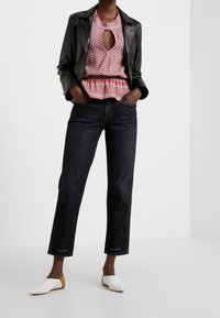 Black jeans with straight-leg cut, paired with a patterned pink and red top featuring a keyhole neckline and ruffled hem, under a black leather jacket. White flat shoes complete the outfit.