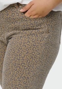 Traperice s leopard uzorkom izrađene od trapera, sadrže smeđu podlogu s tamnosivim mrljama, prednji džep i metalne detalje na struku.