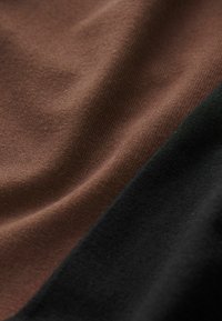 Puuvillane kangas, millel on pruunid ja mustad toonid ning sile tekstuur. Äärte ääres on nähtavad õmblused.