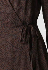 Brauner Stoff mit einem schwarzen Leopardenmuster. Das Wickeldesign hat einen gebundenen Knoten in der Taille und präsentiert eine glatte, weiche Textur.