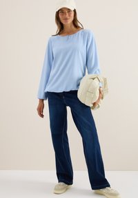 Lichtblauwe blouse met lange mouwen en een ronde hals, gecombineerd met donkerblauwe wijde jeans en een crèmekleurige pufferjack.