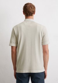 Jasno-beżowa koszula z krótkim rękawem, wykonana z miękkiego materiału, o prostym kroju i z zagiętym kołnierzykiem. Brak widocznych wzorów lub akcentów.