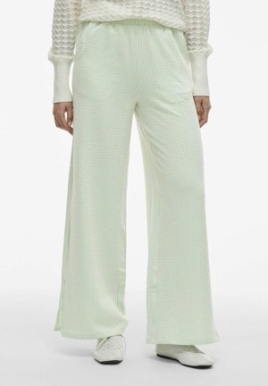 Lichtgroene wijd-uitlopende broek gemaakt van een gestructureerde stof met een subtiele ruitpatroon. Kenmerkt zich door een elastische tailleband en zijslits.