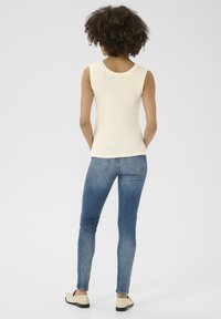 Krämfärgad ribbad linne med rund halsringning, kombinerad med åtsittande blå jeans och beige skor, sedd bakifrån.