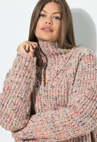 Chunkig, stickad tröja i beige med färgglada prickar av rosa, orange och lila; har en halv-dragkedjekrage och lösa ärmar.
