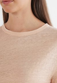 Ljus persikofärgad kortärmad skjorta i ett mjukt, texturerat tyg med rund halsringning. Materialet verkar vara andningsbart och lätt.