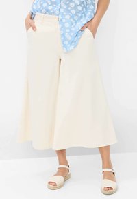 Pantalons larges crème en tissu léger, dotés d'un design fluide, de poches latérales et d'une finition lisse et simple. Assortis avec des espadrilles beige.