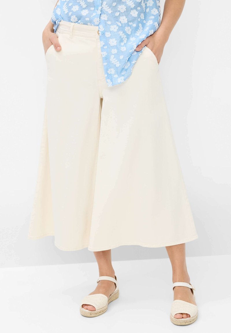 Pantalons larges crème en tissu léger, dotés d'un design fluide, de poches latérales et d'une finition lisse et simple. Assortis avec des espadrilles beige.