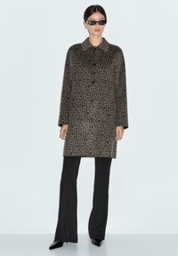 Grey leopard print coat with a collar, featuring black buttons, paired with black flared pants and shiny black shoes.