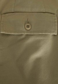 Tessuto beige con una texture morbida, caratterizzato da una chiusura a bottone e un dettaglio con tasca a risvolto. Il materiale è liscio con una fine trama.