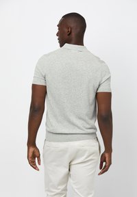 Grå kortärmad polo med texturerat stickat tyg, ribbad krage och ärmslut, samt en figurnära design, bärs med ljusa byxor.