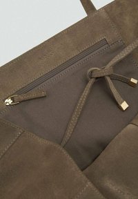 Borsa a tote in suede marrone con un interno in tessuto liscio, dotata di una tasca con zip e una chiusura a coulisse con dettagli in oro.