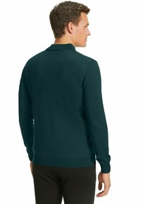 Maglione lungo a maniche, di colore verde scuro, realizzato in materiale a maglia fine, con scollatura rotonda e orlo a coste; texture piatta senza motivi visibili.