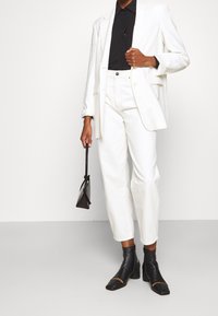 Blazer blanca a medida sobre un polo negro, combinado con pantalones rectos blancos y botas de tobillo negras con tacón. Incluye un pequeño bolso negro.