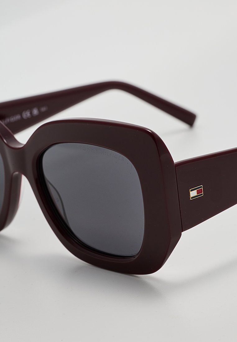 Occhiali da sole rettangolari color bordeaux con lenti scure. Presentano un accento in metallo decorato sulla stanghetta. Realizzati in materiale plastico testurizzato.