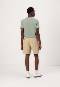 Grøn kortærmet t-shirt, beige shorts og hvide sneakers. Shortsen har en talje og baglommer, med en afslappet pasform.