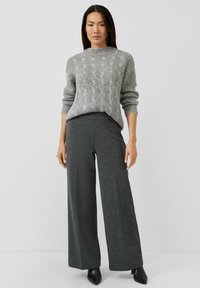 Grauer Strickpullover mit strukturiertem Muster, kombiniert mit weit geschnittenen dunkelgrauen Hosen mit feinem Fischgrätmuster und Ankle-Boots.