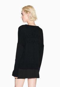 Maglione nero lavorato a maglia con scollo rotondo, maniche lunghe e polsini a costine. Presenta un logo in rilievo sottile sulla schiena.