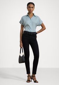 Ανοιχτό μπλε μπλούζα με κοντό μανίκι, μαύρα skinny jeans, υφασμάτινη μαύρη ζώνη, μαύρες φλατ αντλίες με λουράκια, κρατώντας μια μικρή μαύρη τσάντα.