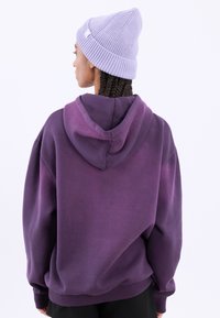 Lilla oversized hettegenser med snor i hetta, myk tekstur og lange ermer. Kombinert med en lys lilla strikket beanie.