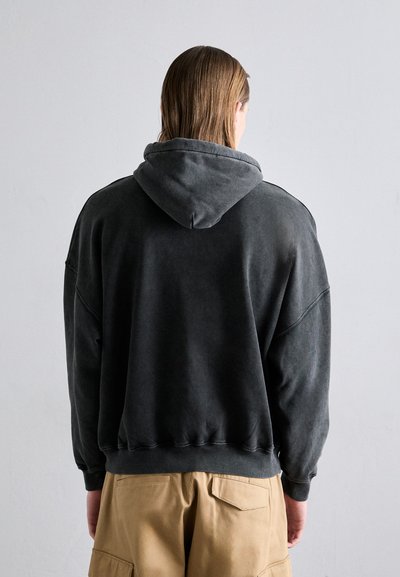 Felpa con cappuccio grigio scuro, di vestibilità rilassata, spalle scese e polsini a costine. Il materiale sembra morbido e leggermente strutturato.