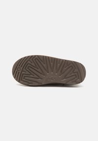 Semelle de chaussure en caoutchouc marron avec un motif de semelle détaillé et le logo UGG. La semelle présente des rainures et des crêtes pour une meilleure adhérence.