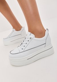 Baskets blanches à plateforme avec une tige en cuir lisse, bout rond, accents gris contrastants et fermeture à lacets. Semelle en caoutchouc épaisse et texturée.