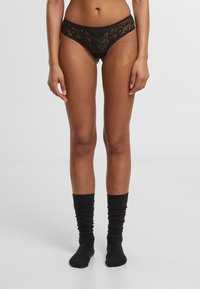 Zwarte kanten slips met een bloemenpatroon en een netstructuur. Gecombineerd met zwarte, slordige katoenen sokken.