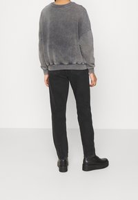 Felpa grigia oversize con collo a coste, abbinata a jeans neri slim-fit e scarpe nere con plateau. Texture morbida e design casual.