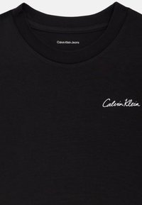 Černé bavlněné tričko s kulatým výstřihem a krátkými rukávy. Na levé části hrudi se nachází bílé vyšívané logo "Calvin Klein Jeans".