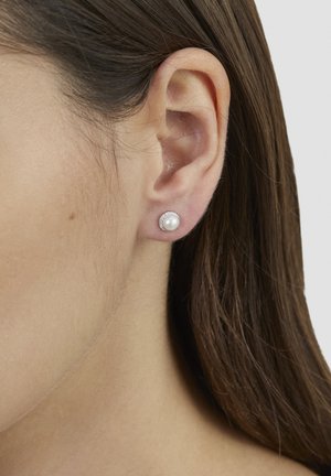 Boucles d'oreilles rondes en perle avec une base couleur argent entourée de petits cristaux clairs, présentées sur un ton de peau neutre.