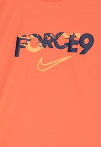 Korall színű póló merész sötétkék "FORCE9" grafikával és sárga Nike logóval. Puha anyag, kényelmes illeszkedéssel és kerek nyakkivágással.