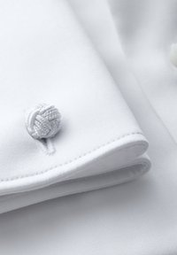 Tessuto bianco con una superficie liscia, caratterizzato da bordi ripiegati e un accento decorativo a nodo bianco. La cucitura è ordinata e consistente.