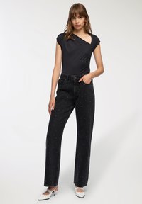 Body nero con maniche corte, abbinato a jeans neri a vita alta caratterizzati da decorazioni bianche sparse e una vestibilità ampia.