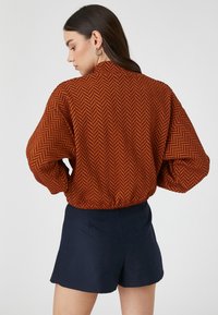 Bluzka z rustykalnym wzorem jodełki, poduszkowe rękawy, elastyczny dół, połączona z ciemnoniebieskimi szortami. Gładka tekstura, casualowy krój.