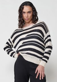 Pulover tricotat cu dungi negre și crem, cu o croială lejeră, decolteu larg și tiv ribflat. Țesătura texturată adaugă detalii designului.