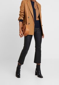 Blazer marrón a medida sobre una blusa de bloques de color beige y azul marino, combinado con pantalones de piel negros recortados y botas de tacón negro hasta el tobillo. Bolsa marrón.