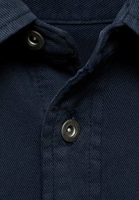 Navy blue fabric close-up of a shirt collar with a metal snap button. Features subtle texture and stitching details.