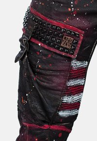 Zwarte denim broek met rode en witte verfspetters, textuuraccenten, zijstuds en een merklabel op de tailleband.