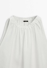 Blouse sans manches blanche avec un col froncé. Tissu léger et lisse ; présente une petite étiquette cousue à l'intérieur. Design simple et fluide.