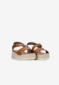 Sandalias de esparto de cuero marrón con correas en X, plataforma envuelta en yute y cierre de hebilla. Suela plana con detalles de costura.