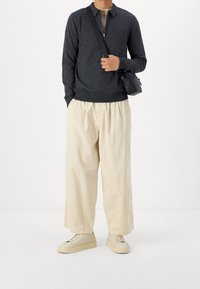 Mörkgrå tröja med dragkedjekrage, i kombination med löst sittande beige byxor. Svart axelväska och ljusa sneakers komplettar outfiten.