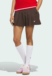 Brown pleated skirt with side pockets and a small red logo, paired with knee-high white socks and pink sneakers with a tan sole.