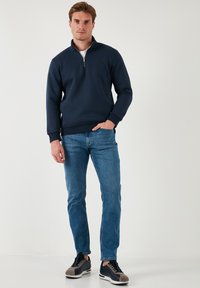 Mornarska polu-zip dukserica, tkanina od kombinacije pamuka, rebrasti manžeti i donji rub, uparena sa svijetloplavim trapericama i crnim tenisicama sivi detalji.