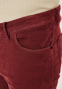 Rote Cordhosen mit strukturierter Oberfläche, Fünf-Taschen-Design und kontrastierendem Bund. Sichtbare Nähte entlang der Kanten.