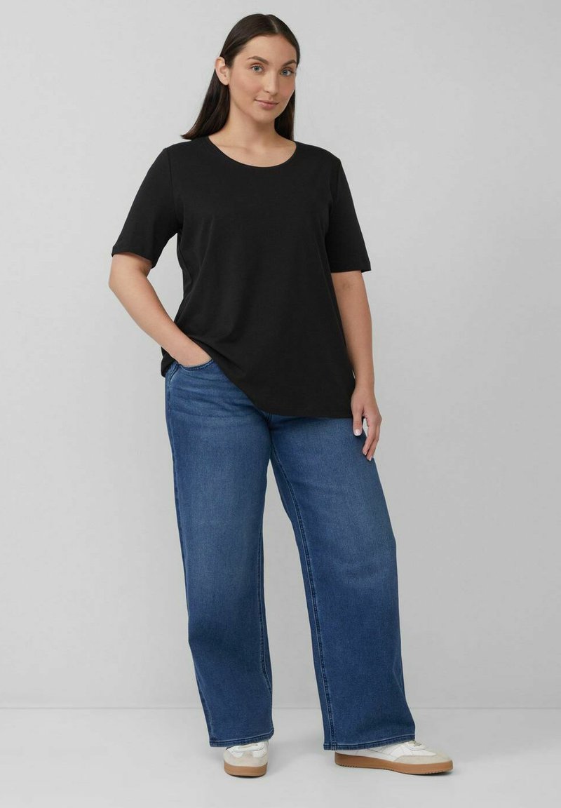 Black cotton t-shirt with short sleeves paired with wide-leg blue denim jeans. White sneakers with light tan soles. Minimal design.