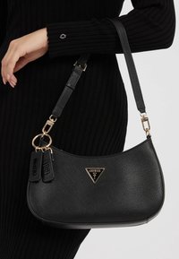 Borsa a tracolla nera in materiale sintetico con una forma strutturata, caratterizzata da un logo triangolare, dettagli in hardware dorato e una tracolla regolabile.