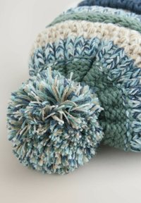 Bonnet d'hiver tricoté multicolore avec du fil bleu, beige et vert, doté d'un grand pompon sur le dessus.