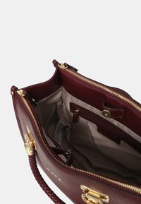Borsa in pelle borgogna con manico intrecciato, hardware dorato e interno beige dotato di tasche con zip e tasche a soffietto per l'organizzazione.